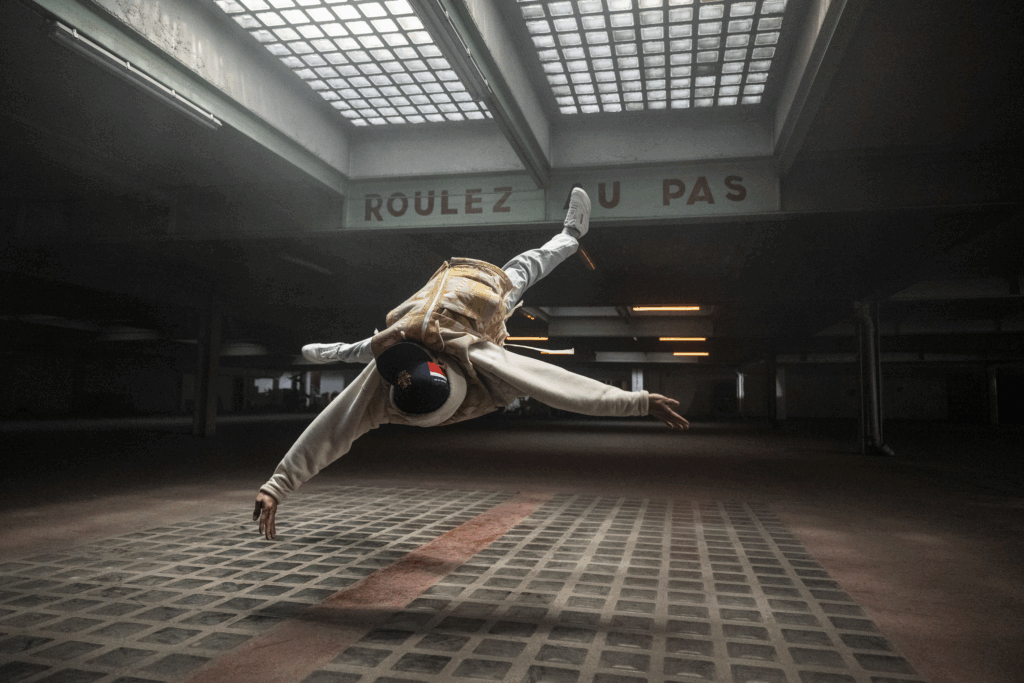 Breaking dancer suspended mid-air in a parking garage, industrial lighting — photo by Little Shao, Urban Photo 2025 at Quai de la Photo