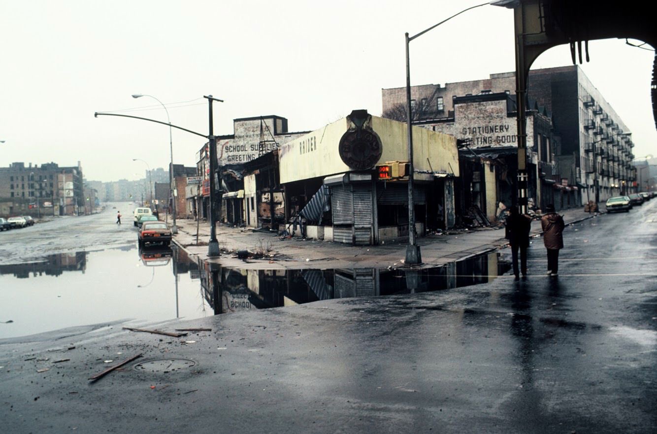 Rue du Bronx détrempée, façades délabrées et reflets sur l’asphalte — photographie de Martine Barrat, années 1970-80, Urban Photo 2025