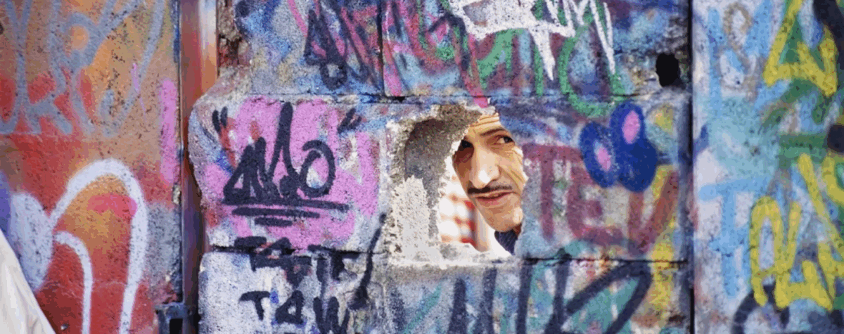 Homme regardant à travers un trou dans un mur couvert de graffitis — photographie de Gérard Guittot, Urban Photo 2025