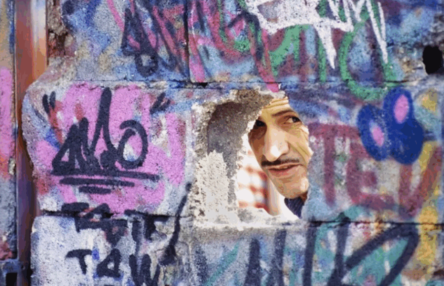 Homme regardant à travers un trou dans un mur couvert de graffitis — photographie de Gérard Guittot, Urban Photo 2025