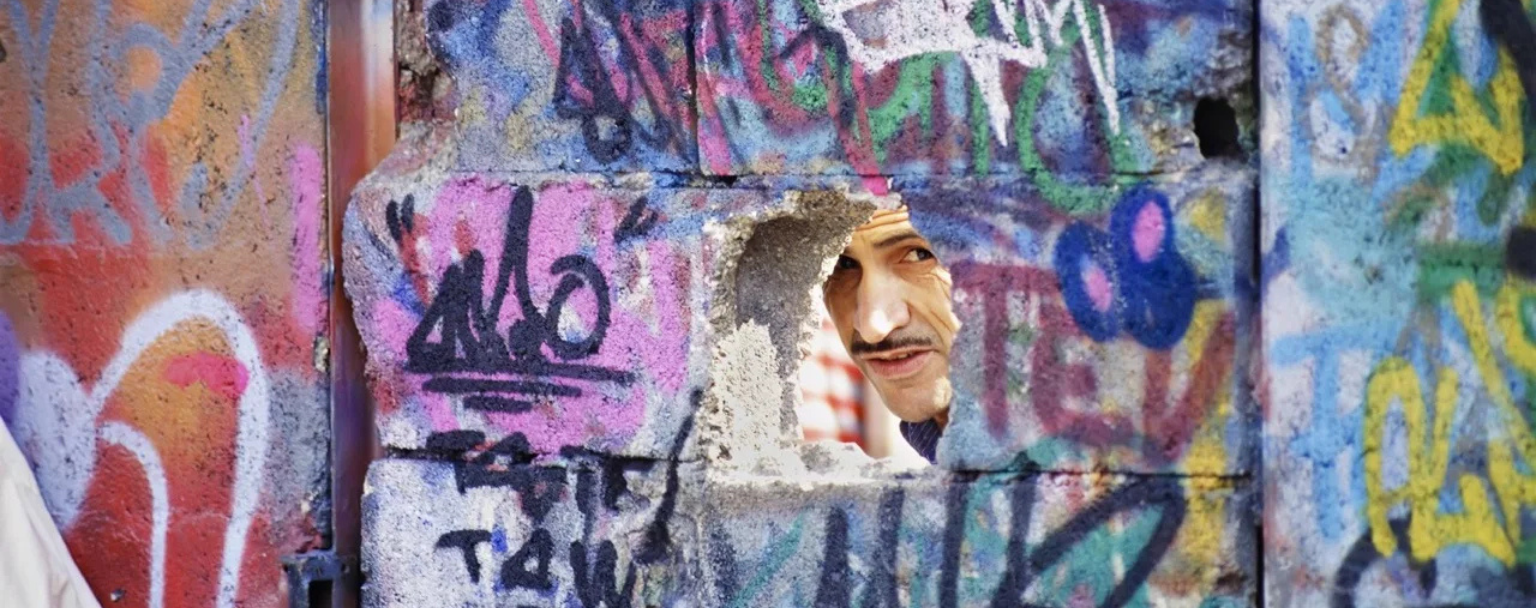 Homme regardant à travers un trou dans un mur couvert de graffitis — photographie de Gérard Guittot, Urban Photo 2025