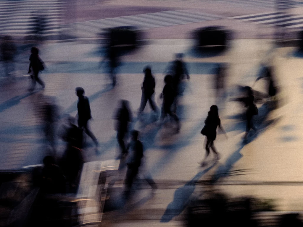 Groupe de passants flous projetant de longues ombres, sensation de flux urbain.
