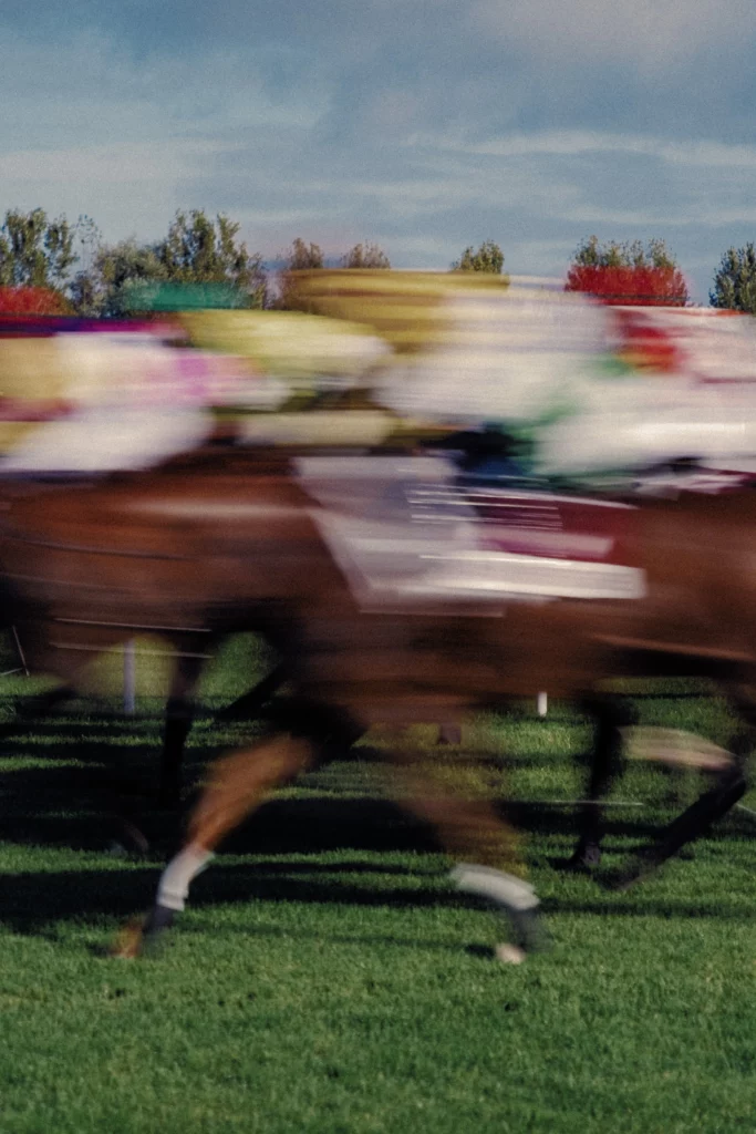 Chevaux et jockeys filés en course, traînées colorées sur l’herbe.