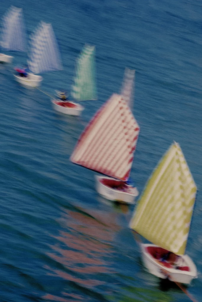 Petits voiliers aux voiles rayées floutées, filé sur la surface bleue.