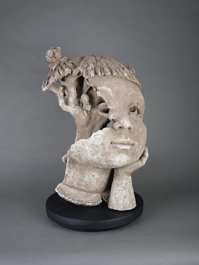Sculpture d’un visage d’enfant partiellement ouvert laissant apparaître un arbre, terre cuite texturée, sur socle noir. Les liens qui nous tissent série présentée lors de la rétrospective de Valem à l'espace Saint Pierre des Minimes de Compiègne jusqu'au 30 novembre article art mag
