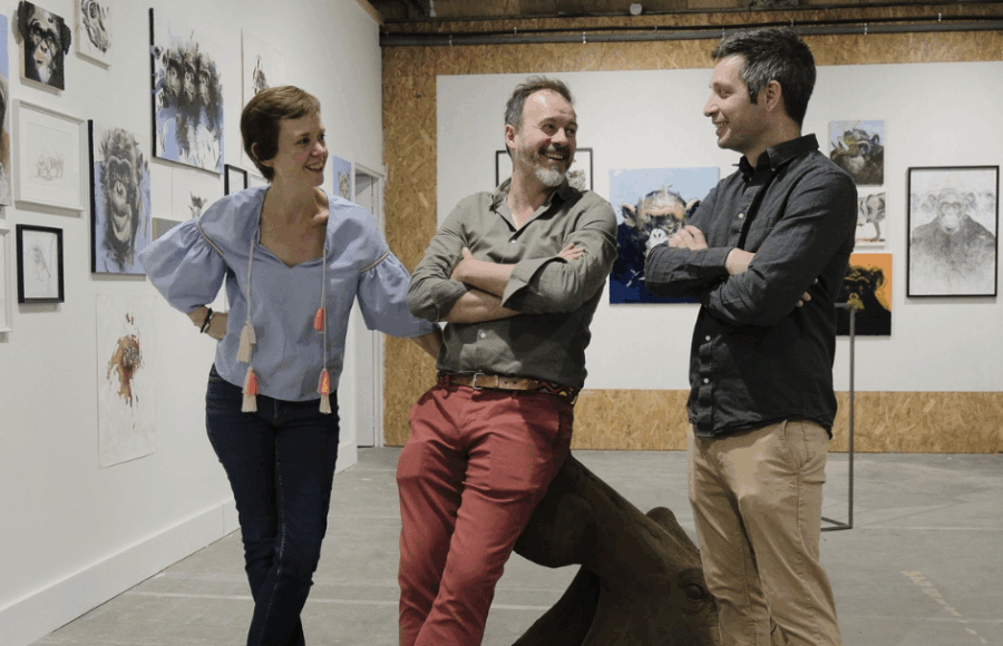 Sarah Scouarnec, Pierre-Jean Chabert et Thibault Jandot discutant devant une série d’œuvres animalières exposées aux Ateliers de la Morinerie à Saint-Pierre-des-Corps. À gauche, plusieurs peintures représentant des chimpanzés ; au centre, les trois artistes échangent dans une ambiance conviviale au cœur de l’espace d’exposition.