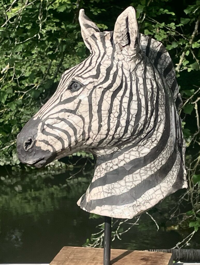 Sculpture animalière de Régis Sinoquet — tête de zèbre en céramique à craquelures, profil, fond de nature.