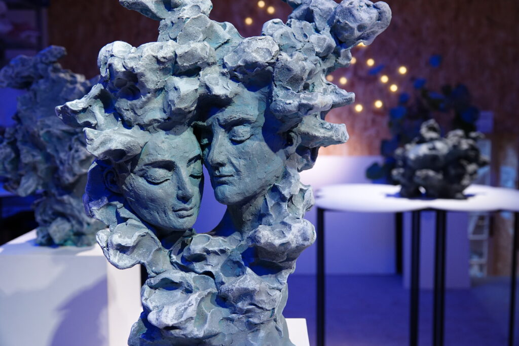 Sculpture en terre cuite patinée de Sarah Scouarnec représentant deux visages entrelacés, entourés de formes organiques. Une œuvre onirique aux tonalités bleues, inspirée du surréalisme et de la mythologie, exposée aux Ateliers de la Morinerie.
