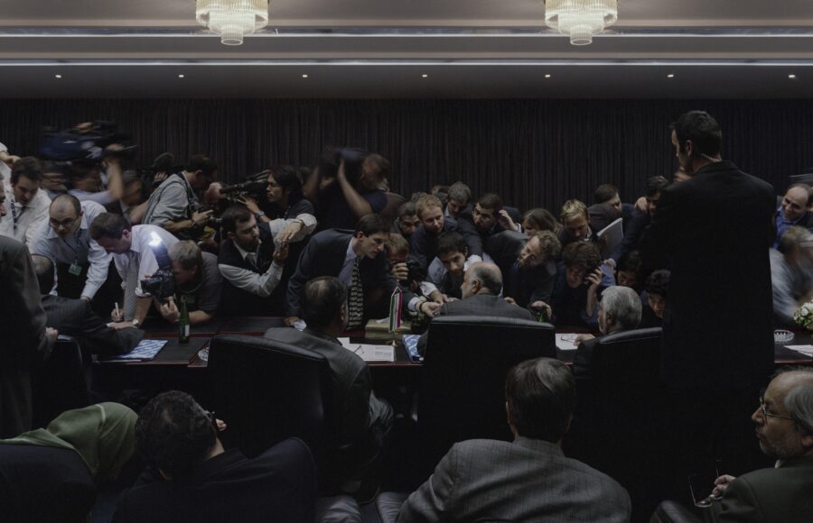 Photographie de Luc Delahaye montrant une conférence de presse dense et chaotique où journalistes, caméras et dirigeants s’entassent autour d’une table. Œuvre emblématique du rapport entre pouvoir, médias et mise en scène du réel. Exposition Le bruit du monde, Jeu de Paume, 2025. Article Magazine art mag