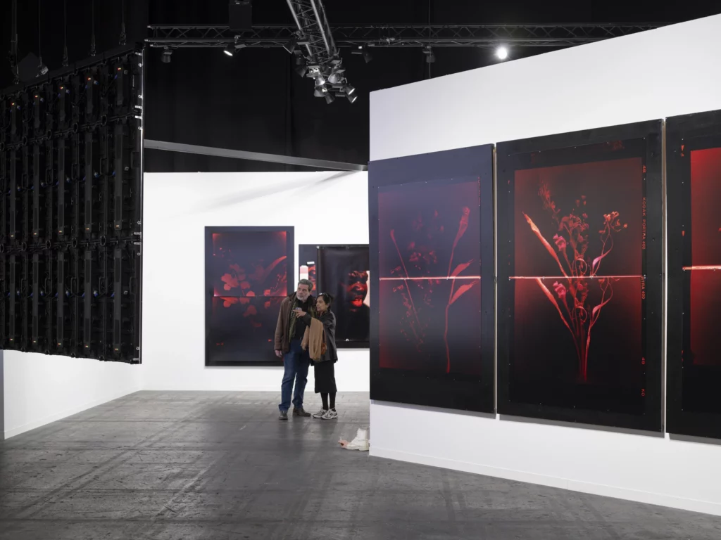 Art Genève exposition 2025 : visiteurs observant de grandes œuvres photographiques rouges dans un stand d’art contemporain, au cœur du salon à Palexpo Genève.