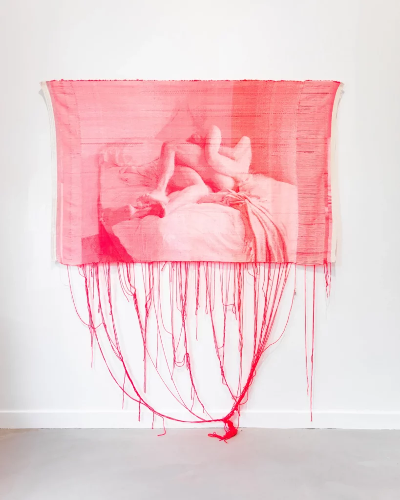 Tapisserie rose représentant un corps allongé sur un lit, fils rouges tombant au sol – œuvre « A Flash of Heat » (2024) de l’artiste Mia Weiner, présentée à Paris Photo 2025, Homecoming Gallery – magazine ART MAG.