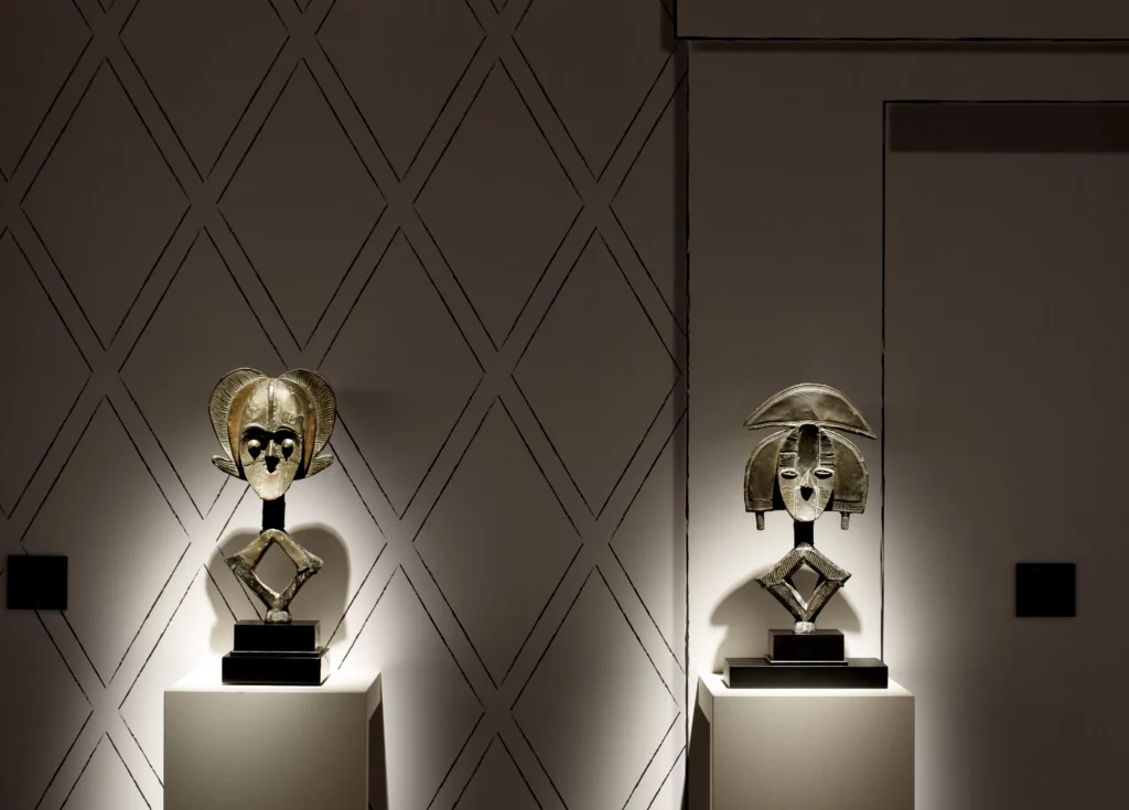 Deux figures reliquaires Kota du Gabon en cuivre et laiton, présentées par Dalton Somaré à BRAFA 2026. Sculptures traditionnelles africaines au style géométrique emblématique, exposées sur socles et éclairées dans un espace muséal.