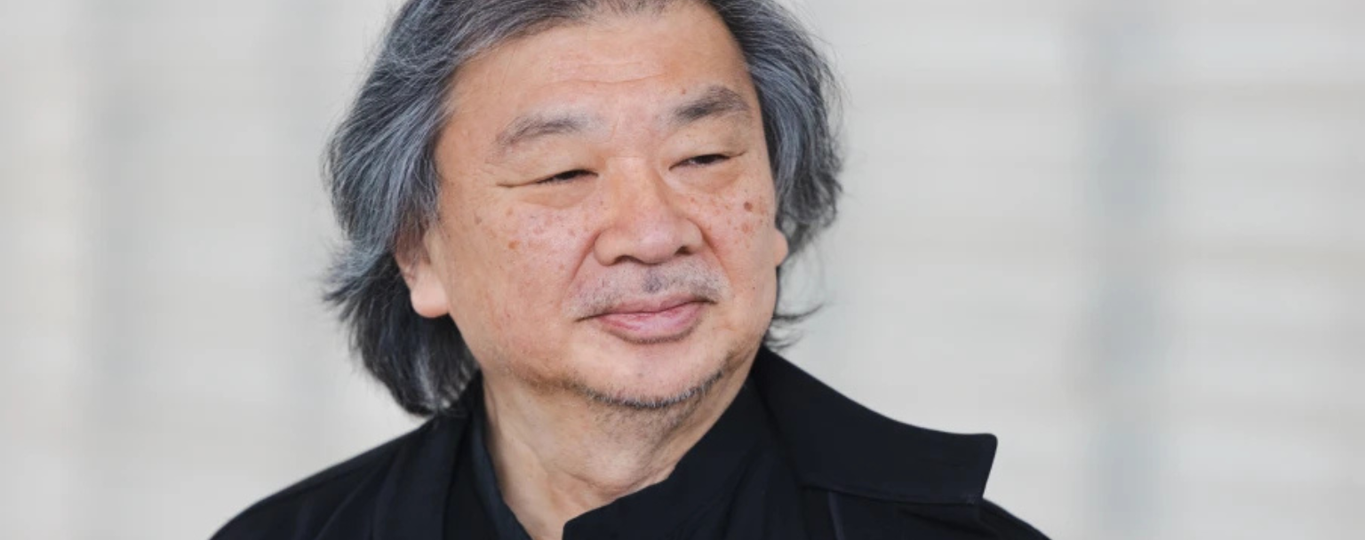 Portrait of Shigeru Ban, Japanese architect and Pritzker Prize laureate, photographed in three-quarter view, wearing black, against a light background.