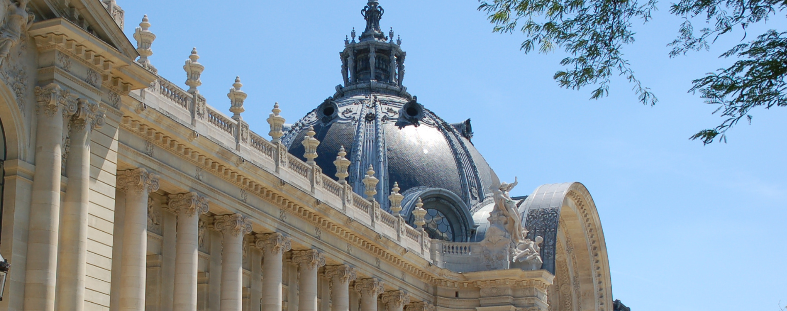 Facade of the Petit Palais in Paris, with its monumental columns and ornate dome, under a blue sky.