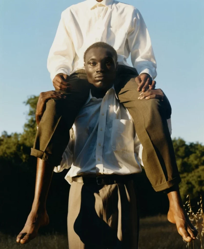 Portrait de deux hommes noirs, l’un assis sur les épaules de l’autre, dans une lumière dorée et un paysage naturel, photographie de Tyler Mitchell.