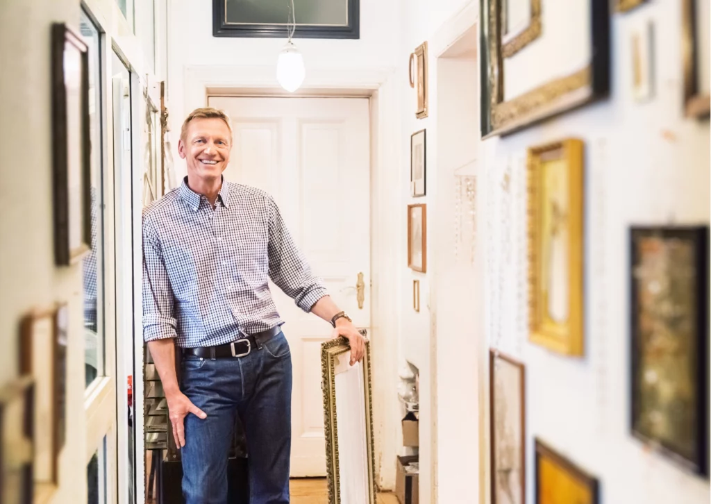 Galeriste et expert en art dans un espace de collection, entouré de cadres et d’œuvres d’art, illustrant le marché de l’art, la collection privée et l’expertise artistique contemporaine.