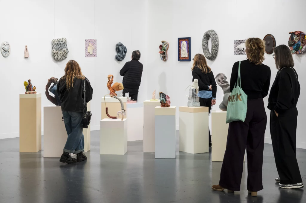 Vue d’ensemble de ceramic brussels avec stands d’art contemporain, sculptures céramiques colorées, public en visite dans les halls industriels lumineux de Tour & Taxis.