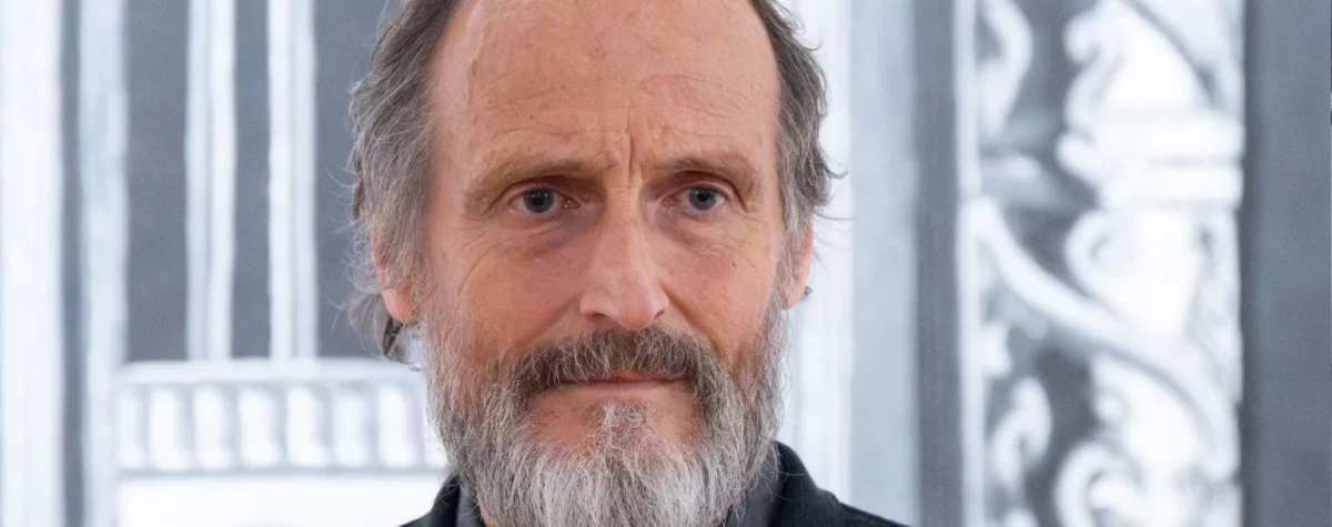 Portrait d’un homme barbu à l’expression neutre, photographié en intérieur devant un décor graphique en noir et blanc, dans le cadre d’un événement lié à l’art contemporain et à la céramique. Art mag