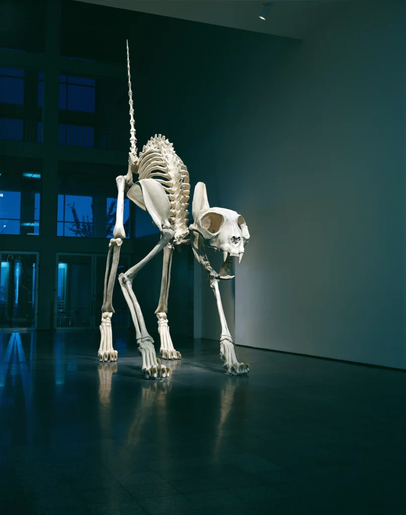 Monumental sculpture Felix by Maurizio Cattelan depicting a giant cat skeleton displayed in a modern museum space, contemporary art installation at the Centre Pompidou-Metz, with dramatic lighting emphasizing the imposing structure of the artwork. Art mag
