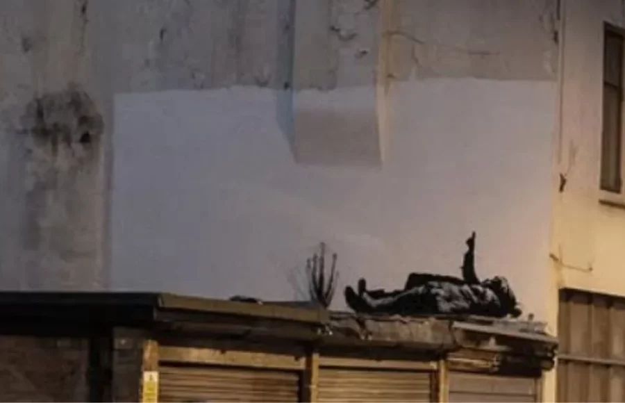Pochoir de Banksy à Londres représentant deux enfants allongés sur un toit, l’un pointant le ciel, sur un mur urbain délabré.