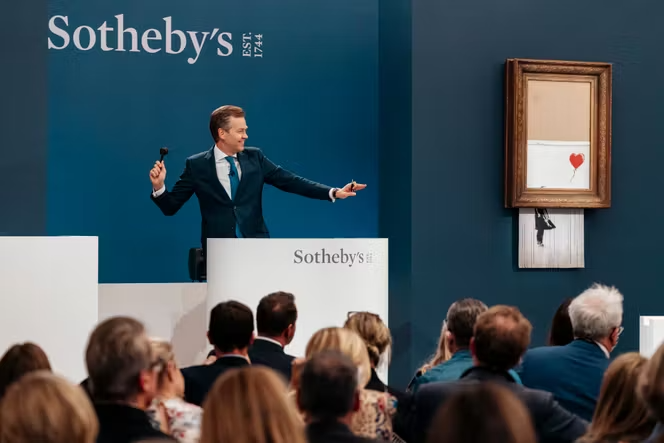 Vente aux enchères chez Sotheby's avec une œuvre de Banksy encadrée et un commissaire-priseur devant les collectionneurs.