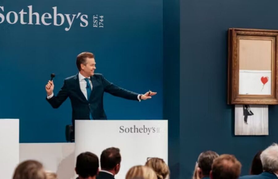 Vente aux enchères chez Sotheby's avec une œuvre de Banksy encadrée et un commissaire-priseur devant les collectionneurs.