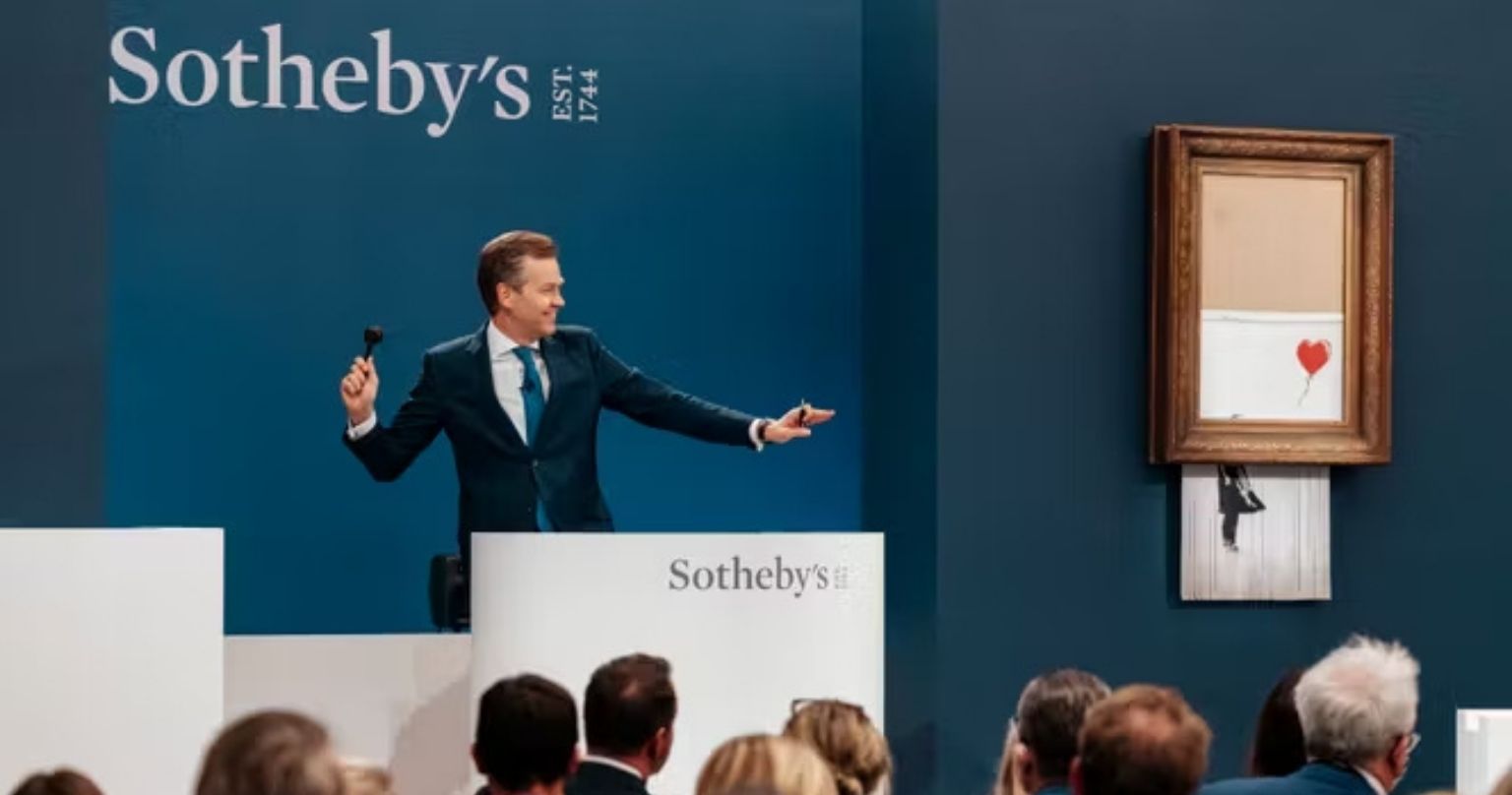 Vente aux enchères chez Sotheby's avec une œuvre de Banksy encadrée et un commissaire-priseur devant les collectionneurs.